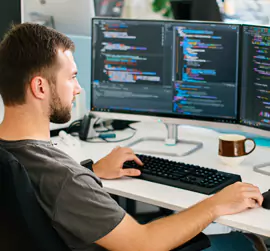 Person coding at a dual-monitor workstation in a modern office.