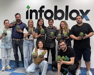 Ein Team von neun Mitarbeitern, das lächelnd Terrarien in den Händen hält und vor einer Wand mit dem Infoblox-Logo posiert.