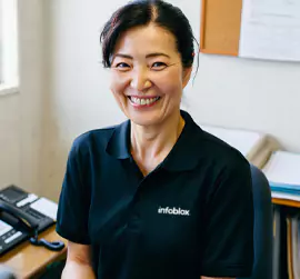Lächelnde Frau in einem Infoblox-Poloshirt an ihrem Schreibtisch.