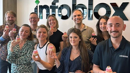 Group of coworkers smiling and holding cupcakes in front of the Infoblox logo.