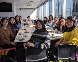 A group of people gathered around a table enjoying tea and snacks, smiling in natural light.